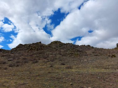 Mavi Gök 'ün altında kabarık bulutlu kayalık dağ manzarası 
