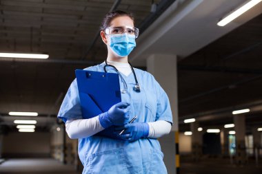 PPE üniforması, güvenlik gözlükleri ve yüz maskesi takan sağlık görevlisi, gezici test merkezinde pano tutuyor, PCR Coronavirus COVID-19 virüsü tespit ediyor.