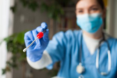 Beyaz kadın NHS doktoru elinde pamuklu çubuk, doktor muayenehanesinde burun ve ağız örneği, hasta PCR test randevusu, Coronavirus COVID-19 küresel salgın krizi