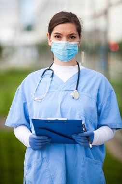 Hastanenin önündeki yorgun ve yorgun kadın NHS doktorunun portresi, odak arkaplanı bulanıklığı, Coronavirus COVID-19 salgın krizi, çok çalışan tıbbi personel 