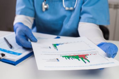 Koruyucu eldivenler giyen doktor COVID-19 grafik verilerini analiz ediyor, Coronavirus küresel salgın krizi, hasta sayısını, ölü sayısını, ölüm oranını, ölüm oranını gösteren istatistikler