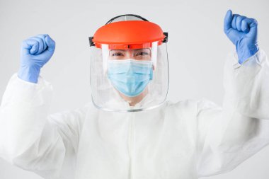 Coronavirus COVID-19 küresel salgın salgını, kişisel koruma ekipmanlarında muzaffer doktor ya da hemşire, yumruklarını sıkan ve kollarını havada kaldıran, mutlu, hasta iyileşme sürecinden sonra heyecanlanan ve heyecanlanan