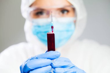 Doctor or lab scientist in personal protective equipment holding syringe jab full of blood plasma,focus on single drop dripping out of the needle tip,healthcare cure treatment and research for vaccine clipart