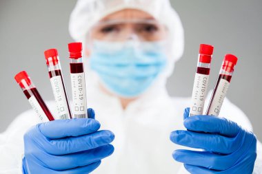 Laboratuvar bilimcisi ya da tıp teknolojisi uzmanı koruyucu giysi giyiyor ve maske tutuyor deney tüpü boş, Coronavirus hasta kan örneği, COVID-19 virüs hastalığı PCR DNA analizi görselleştirme