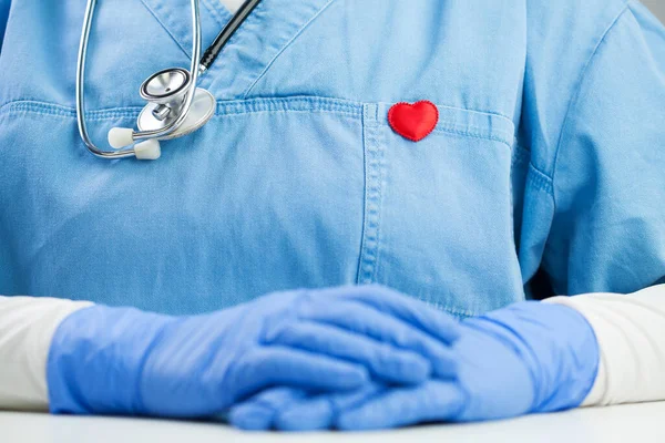 医師の青い制服を着て聴診器と小さな赤いハートバッジピン 詳細を閉じる オフィスでGpや心臓病 デスクに座って コロナウイルスCovid 19世界的なパンデミック発生危機 — ストック写真