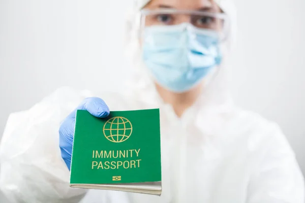 Medical UK healthcare security officer worker in personal protective equipment holding green immunity passport ID card,risk free certificate document concept,health record proof of patient recovery