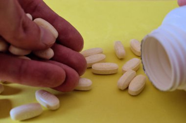 İçinde haplar olan bir kutuyu sarı arka planda 23.2021 numaralı kutunun içine boşaltmak.