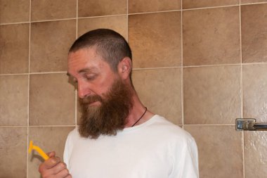 Vaduz, Lihtenştayn 30 Haziran 2021 Büyük sakallı bir adam tıraş makinesiyle banyoda duruyor.