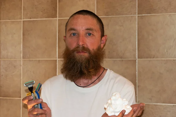 Vaduz, Liechtenstein July 1, 2021 A man with a big beard is standing in a bathroom with his shaver