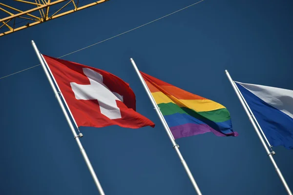 ZURICH, SWITZERLAND, SEPTEMBER 4, 2021 Waving swiss and gender rainbow flag on a rooftop in the city center during a gay pride demo