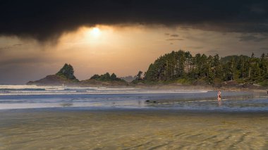 Cox Bay Sahili 'nin üzerinde asılı duran günbatımındaki kara bulutlar ve Kanada' nın Britanya Kolumbiyası, Vancouver Adası 'ndaki Pasifik Kıyısı Ulusal Parkı' ndaki Cox Bay ve Chesterman Sahili arasındaki kayalar.