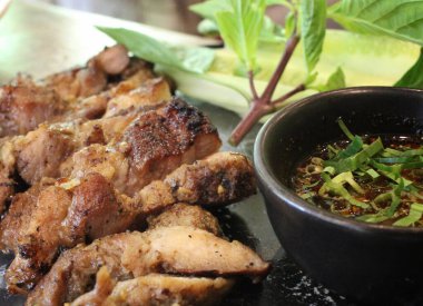 Lezzetli dilimlenmiş domuz bifteği. Bitki ve baharatlı sosla süslenmiş. Gurme restoranındaki siyah taş tabakta servis ediliyor.