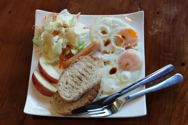 Ev yapımı kahvaltı, taze yumurta, sosis, salata ve tost, beyaz tabakta servis edilen ahşap masa, İngiliz yemekleri, amerikan yemekleri Frhstck, yemek arkaplan reklamları.