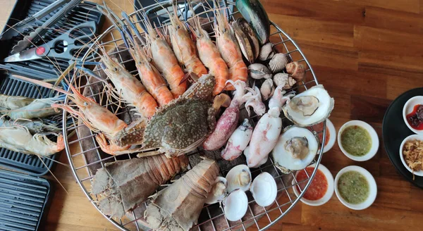 Taze kabuklu deniz ürünleri, karides, yengeç, kalamar, istiridye, ızgara mangal kömürü üzerinde kerevit, yaz açık büfe deniz ürünleri partisinde çeşitli baharatlı soslu ızgara kovası, reklam.