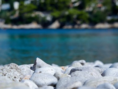 Ön planda beyaz çakıl taşları ve arka planda deniz olan bir plajın makrofotografı. Hırvat sahili..