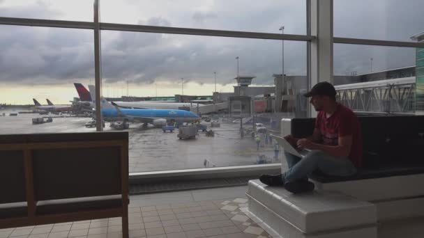 一个男人在机场的出发大厅的笔记本电脑上写东西 背景上的平面 史基浦机场 阿姆斯特丹 — 图库视频影像