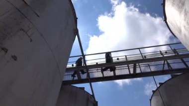 Demir köprünün alt görüntüsü silo tankları deposundan geçiyor ve insanlar üzerinde yürüyor.