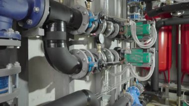 Kazan dairesi içinde büyük tanklar, siyah yalıtılmış boru sistemleri ve tesislerin ısıtılması veya su yönetimi için kullanılan yeşil dolaşım pompaları sergileniyor..