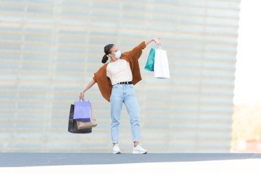 Coronavirus salgını sırasında alışveriş. Alışveriş torbalarını tutan mutlu ve gururlu bir genç kadın..