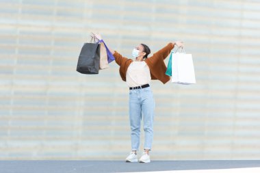 Coronavirus salgını sırasında alışveriş. Alışveriş torbalarını tutan mutlu ve gururlu bir genç kadın..