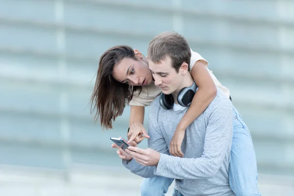 Young Man Carrying His Girlfriend Back Checking Smartphone — Stock Photo, Image