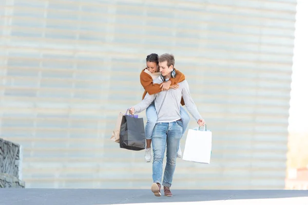 A young man carrying his girlfriend on the back while holding their shopping bags.