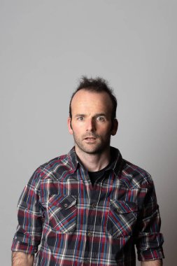 Akıl sağlığı konsepti. Şaşırmış çılgın gevşek adam doğrudan kameraya bakıyor. Kopyalama alanı olan gri arkaplan