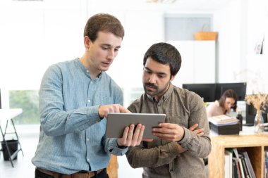 Muhtelif erkek iş arkadaşları ofiste bir tablete bakarken gevezelik edip fikir beyan ediyorlar..