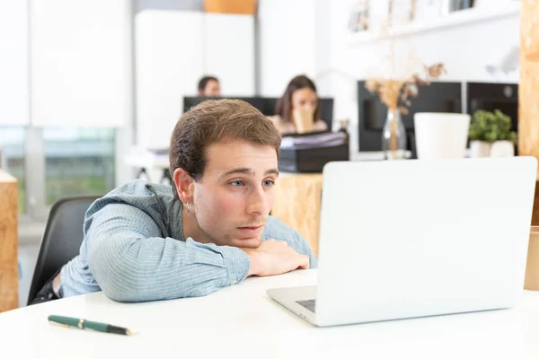 Ofiste dizüstü bilgisayarının önünde sıkılmış ve dağılmış beyaz bir genç..