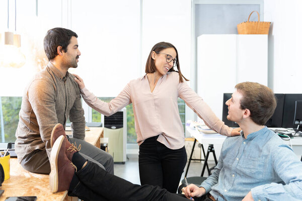 Three diverse young coworkers chatting relaxed at the office.