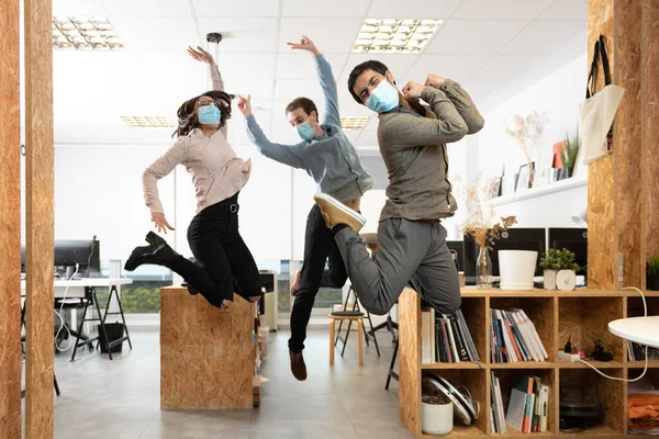 İş yerinde koruyucu maskeler takıp kutlama yapan mutlu iş arkadaşları. Coronavirus salgını sırasında ofiste çalışmak.