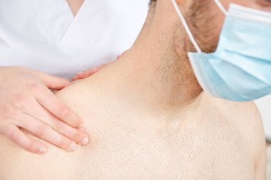 Coronavirus salgını sırasında yüz maskesi takan bir hastanın omzuna masaj yapan bir fizyoterapistin yakın görüntüsü..