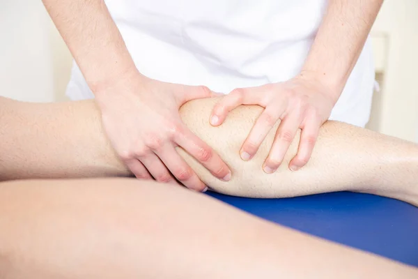 Bir atletin bacağına masaj yapan bir fizyoterapistin elleri..