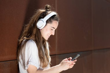 Gülümseyen genç bir kadın paslı metal duvarda izole edilmiş telefonunu kontrol ediyor..