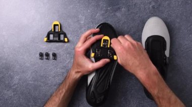View from above of male hands assembling pedal automatic cleats on cycling shoes.