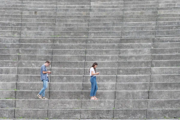 数字成瘾的男人和女人走在看台的楼梯上 看着他们的手机 身体状况不佳 — 图库照片