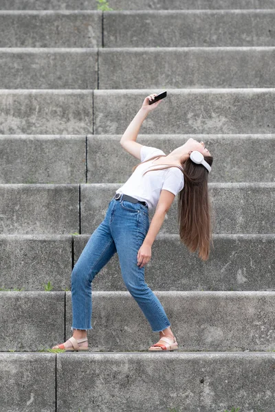 幸せな女性は彼女の電話で音楽を聞いて 一人で壮大なスタンドの階段で踊ります — ストック写真