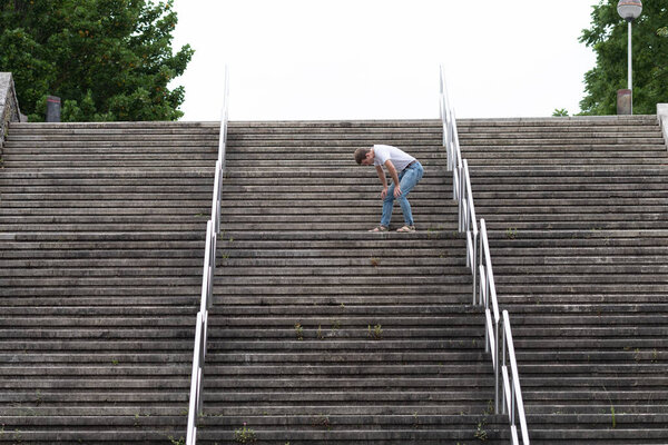 Уставший мужчина поднимается по лестнице как раз перед тем, как подняться на вершину. Трудный путь к успеху и достижению целей