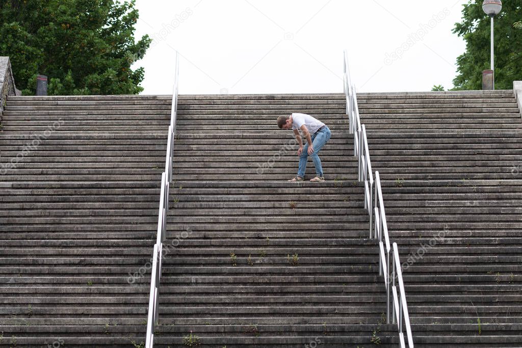 Exhausted man going up on stairs just before reaching the top. Hard way to success and achieving goals concept