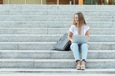 Genç, gülümseyen, dizüstü bilgisayarı üzerinde çalışan, merdivenlerde oturan serbest çalışan..