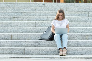 Yoğunlaşmış genç dijital göçebe laptopuyla merdivenlerde oturuyor..
