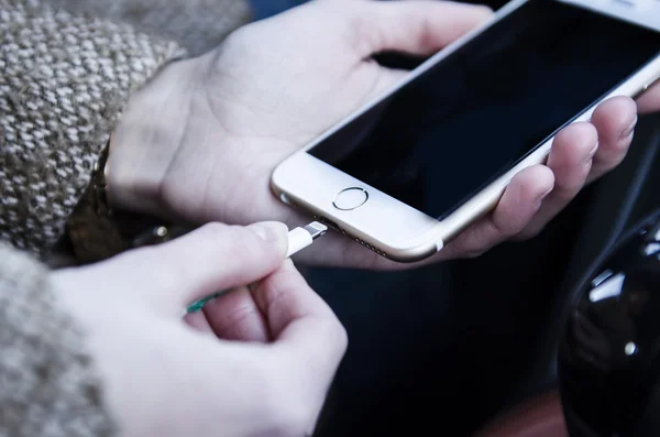 Hands holding white smartphone and plug in — Stock Photo, Image