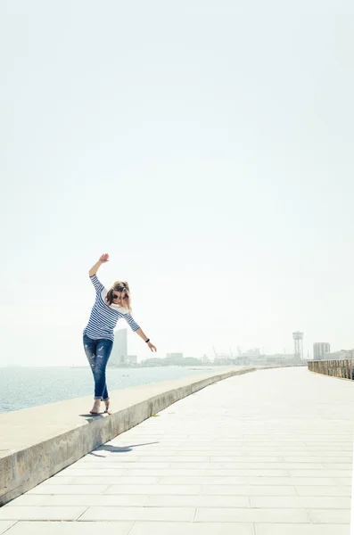 Jonge hipster vrouw lopen in de buurt van de zee weg op Grensweggetje met opgeheven handen. — Stockfoto