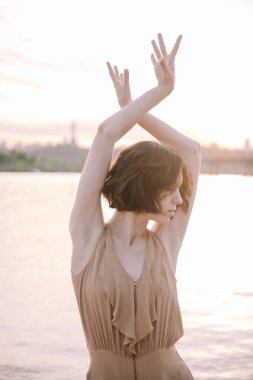 Gün batımında genç bir kadın poz veriyor ve yoga yapıyor.