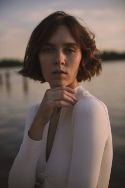 Gün batımında sahile yakın poz veren genç kadın portresi.