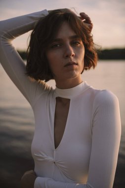 Gün batımında sahile yakın poz veren genç kadın portresi.