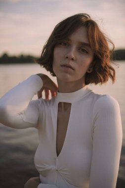 Gün batımında sahile yakın poz veren genç kadın portresi.