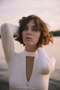 Gün batımında sahile yakın poz veren genç kadın portresi.