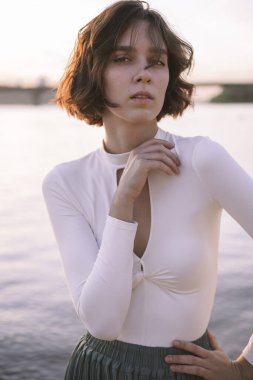 Gün batımında sahile yakın poz veren genç kadın portresi.