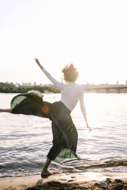 Güzel genç bir kadın poz veriyor ve günbatımı kumsalında yoga yapıyor.